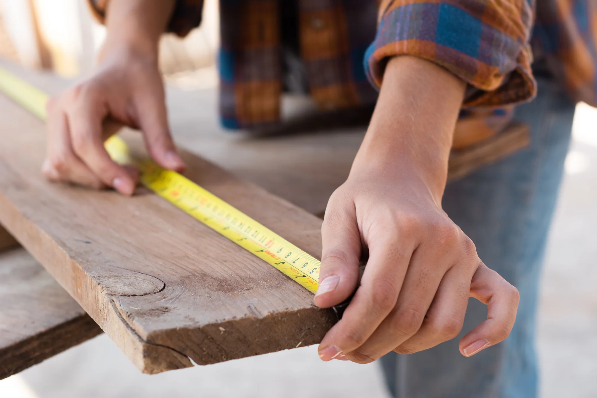 Illustrative carpentry photo: hands measuring a wooden plank